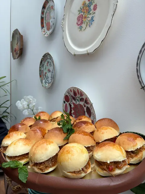 Mini sanduíches de pão macio com carne desfiada, decorados com hortelã